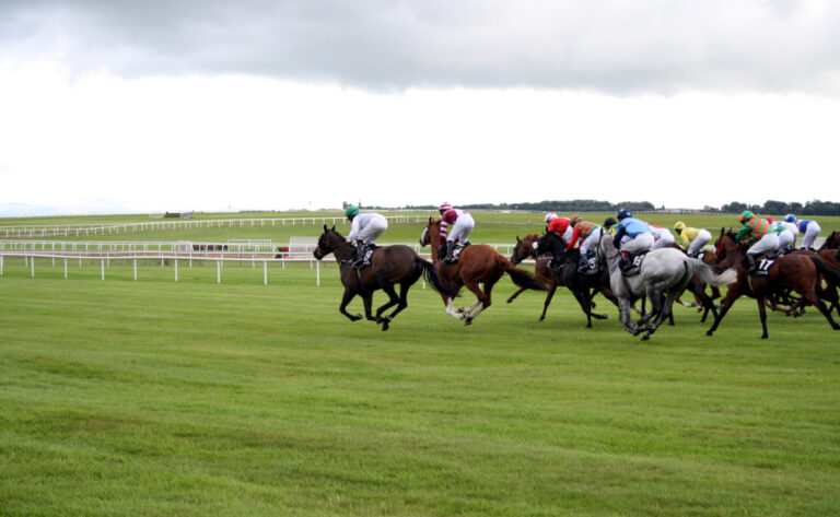 Racehorses running around a track with white railings in the background.
