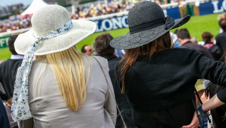 Elegant women with hats watching a horse race.