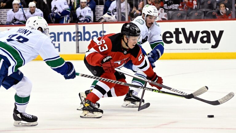 New Jersey Devils left wing Jesper Bratt (63) splits the defense of Vancouver Canucks' Travis Hamonic (27) and Brad Hunt (77) during the first period of an NHL hockey game Monday, Feb. 28, 2022, in Newark, N.J. (AP Photo/Bill Kostroun)