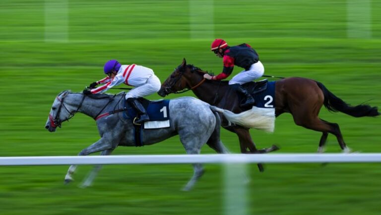 Two horses with mounted jockeys racing on a turf track.