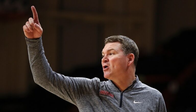 A coach with an Arizona branded tracksuit top holding one finger up in the air