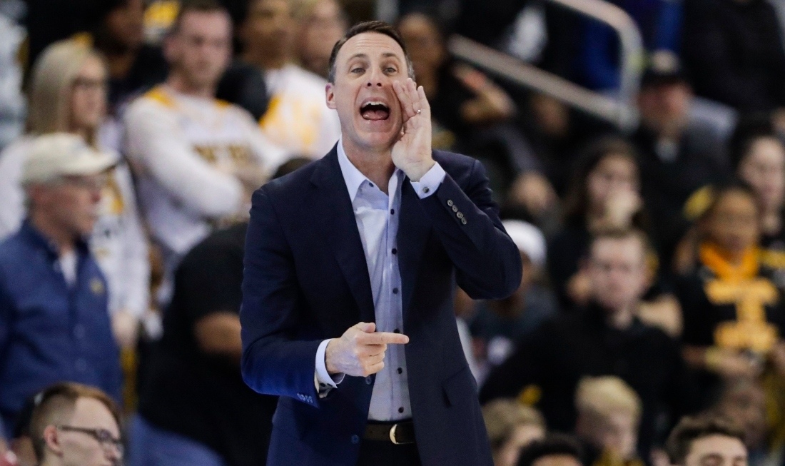 A team manager dressed in a dark blue suit, shouting something at his team on the field