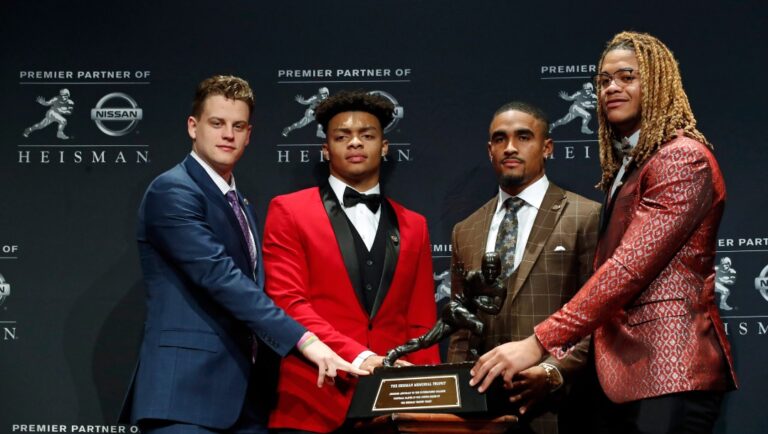 NCAA college football players and Heisman Trophy finalists, from left, LSU quarterback Joe Burrow, Ohio State quarterback Justin Fields, Oklahoma quarterback Jalen Hurts and Ohio State defensive end Chase Young pose for a photo with the Heisman Trophy, Saturday, Dec. 14, 2019, in New York. (AP Photo/Jason Szenes)