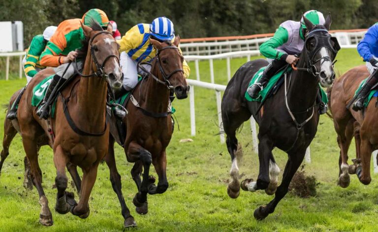 Four horses and jockeys are racing down the track.