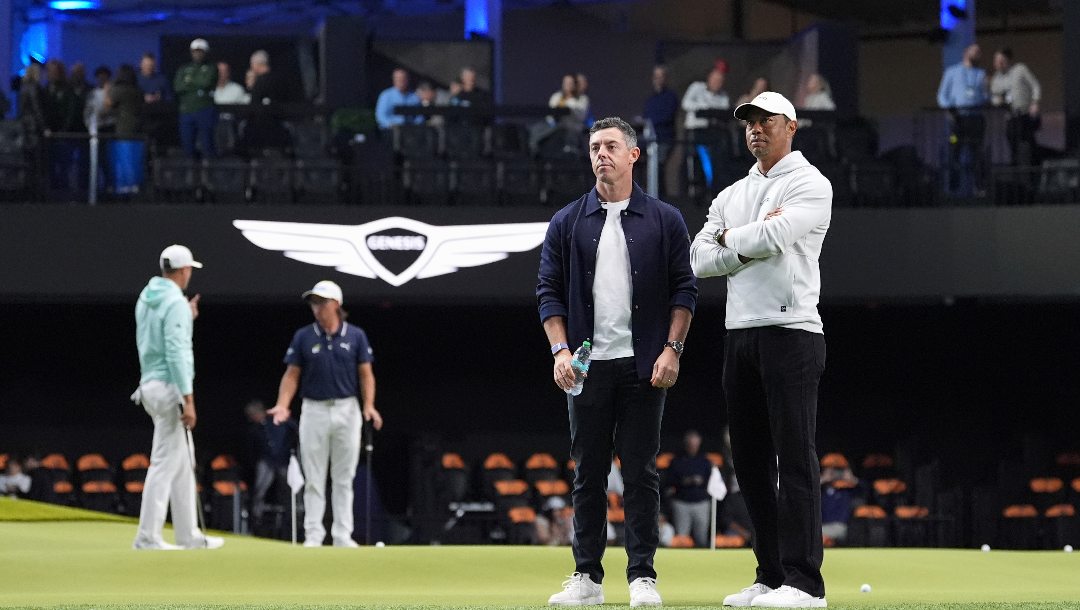 Tiger Woods, right, and Rory McIlroy and stand on the green as they watch New York Golf Club and The Bay Golf Club warmup for the inaugural match of the TMRW Golf League, Tuesday, Jan. 7, 2025, in Palm Beach Gardens, Fla. TGL features six teams of four players competing against each other in a tech-infused arena the size of a football field.