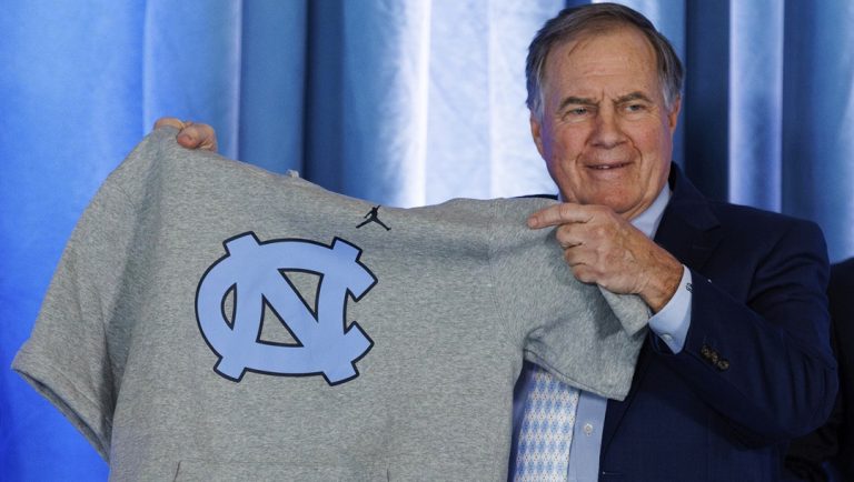 New North Carolina football coach Bill Belichick holds up a UNC branded sleeveless hoodie presented to him during an NCAA college football news conference announcing his hiring, Dec. 12, 2024, in Chapel Hill, N.C.