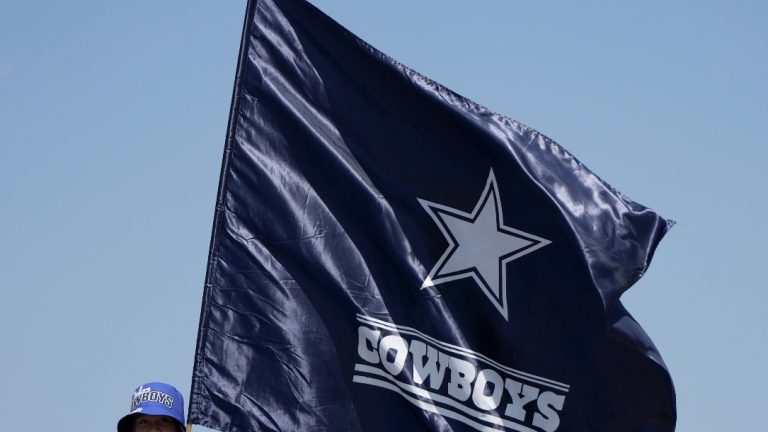 A young fan sands atop a vehicle holding a Dallas Cowboys flag outside Sofi Stadium before a preseason NFL football game between the Dallas Cowboys and Los Angeles Rams, Sunday, Aug. 11, 2024, in Inglewood, Calif. (AP Photo/Gregory Bull)