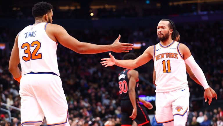 Jalen Brunson #11 reacts with Karl-Anthony Towns #32 of the New York Knicks during the first half of their Emirates NBA Cup Quarterfinal game against the Toronto Raptors at Scotiabank Arena on December 9, 2025 in Toronto, Ontario, Canada.